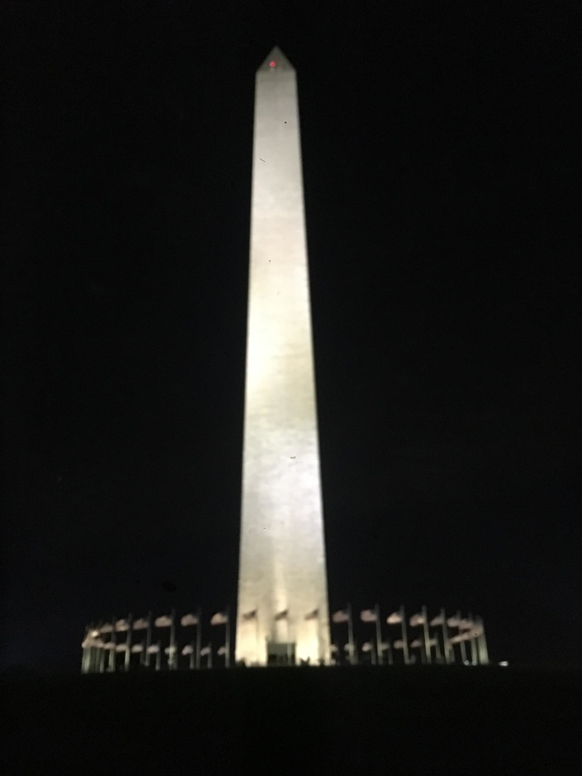Washington Monument illuminated at night, surrounded by flags, with a clear dark sky in the background. Schaeffer Farms mountain bike trail.