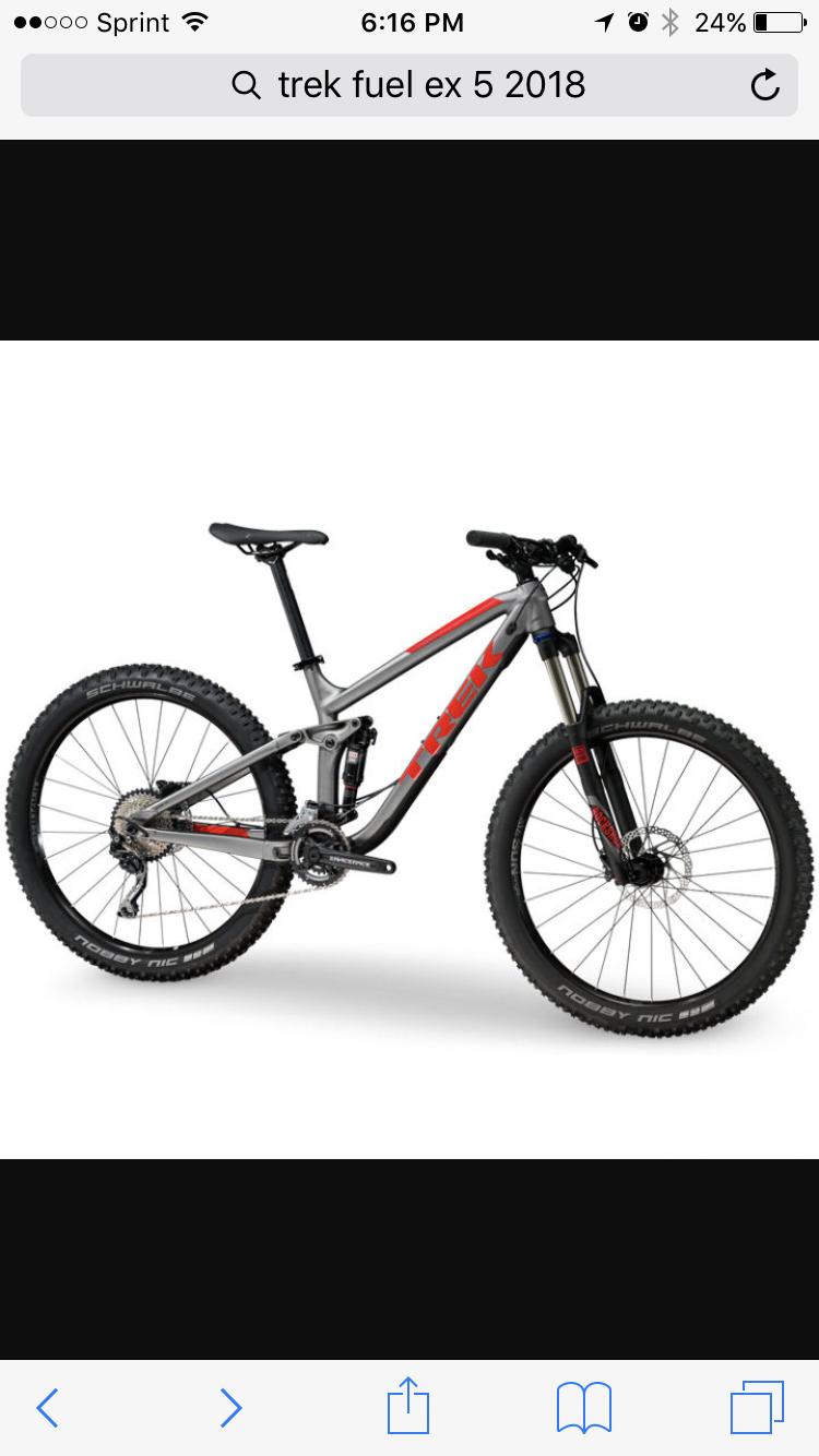 Trek Fuel EX 5: Alt text: A 2018 Trek Fuel EX 5 mountain bike displayed on a white background. The bike features a gray frame with red accents, wide tires, and a front suspension fork, showcasing its design for off-road riding.
