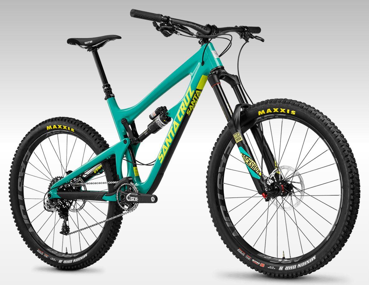 Santa Cruz Nomad: A vibrant turquoise mountain bike with a sleek frame, featuring prominent yellow and black decals. The bike is equipped with wide, knobby tires labeled "MAXXIS," a dropper seat post, and a high-performance suspension fork. The design emphasizes agility and durability, ideal for off-road adventures. The background is a smooth gradient, highlighting the bike's details.