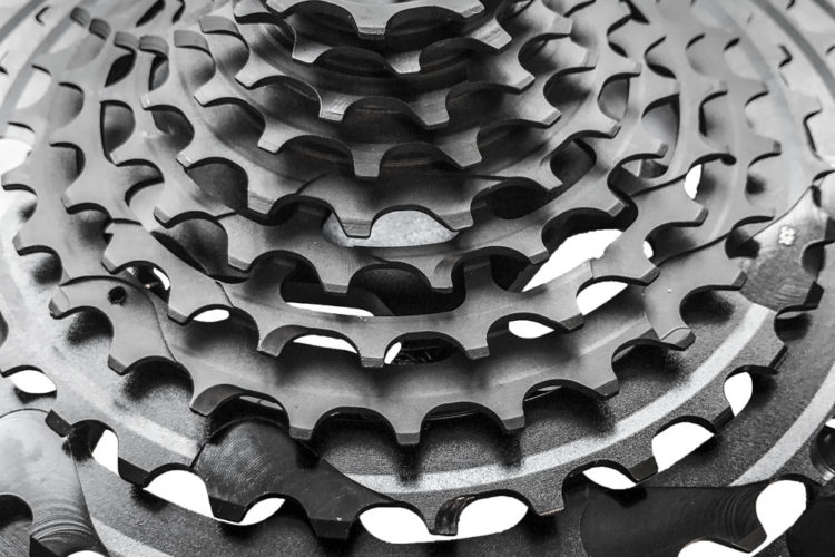 Close-up image of a stack of bicycle cassette sprockets in black, showcasing various sizes and teeth profiles arranged in ascending order. The sprockets have a metallic finish and intricate detailing, highlighting their mechanical design.