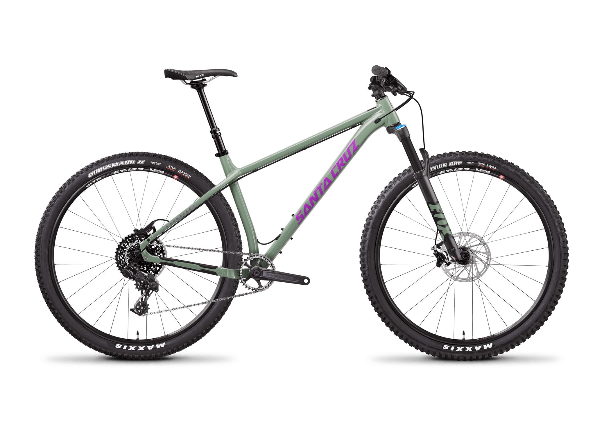 Santa Cruz Chameleon: A side view of a Santa Cruz mountain bike, featuring a sleek green frame and prominent purple branding. The bike is equipped with a front suspension fork, wide knobby tires for off-road traction, and a modern drivetrain setup. The seat is adjustable, allowing for custom height adjustments. The background is plain white, emphasizing the bike's design.