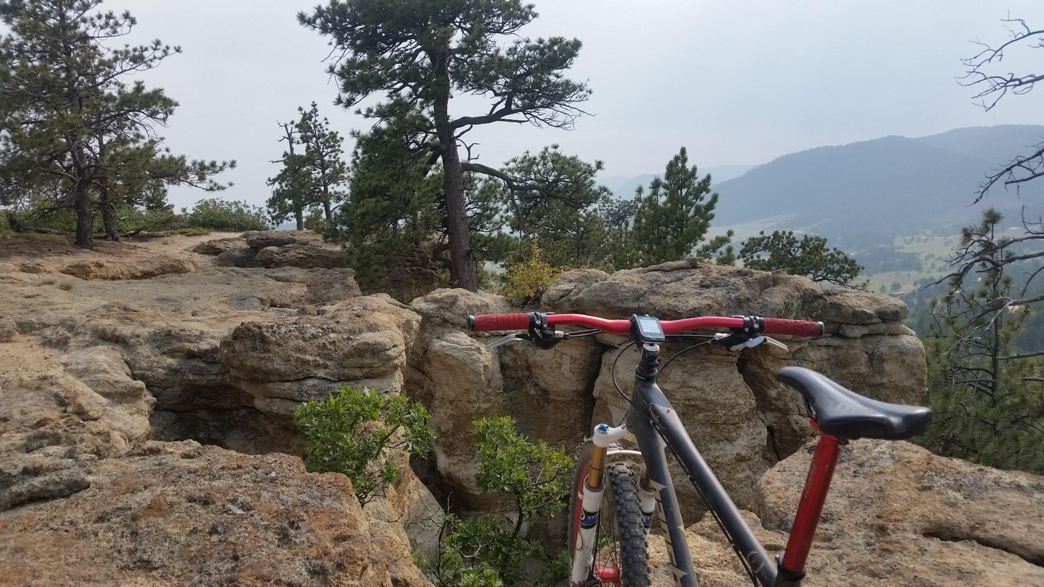 Mountain bike resting on rocky outcrop overlooking a hazy landscape of trees and hills. Spruce Mountain Trail Upper Loop mountain bike trail.