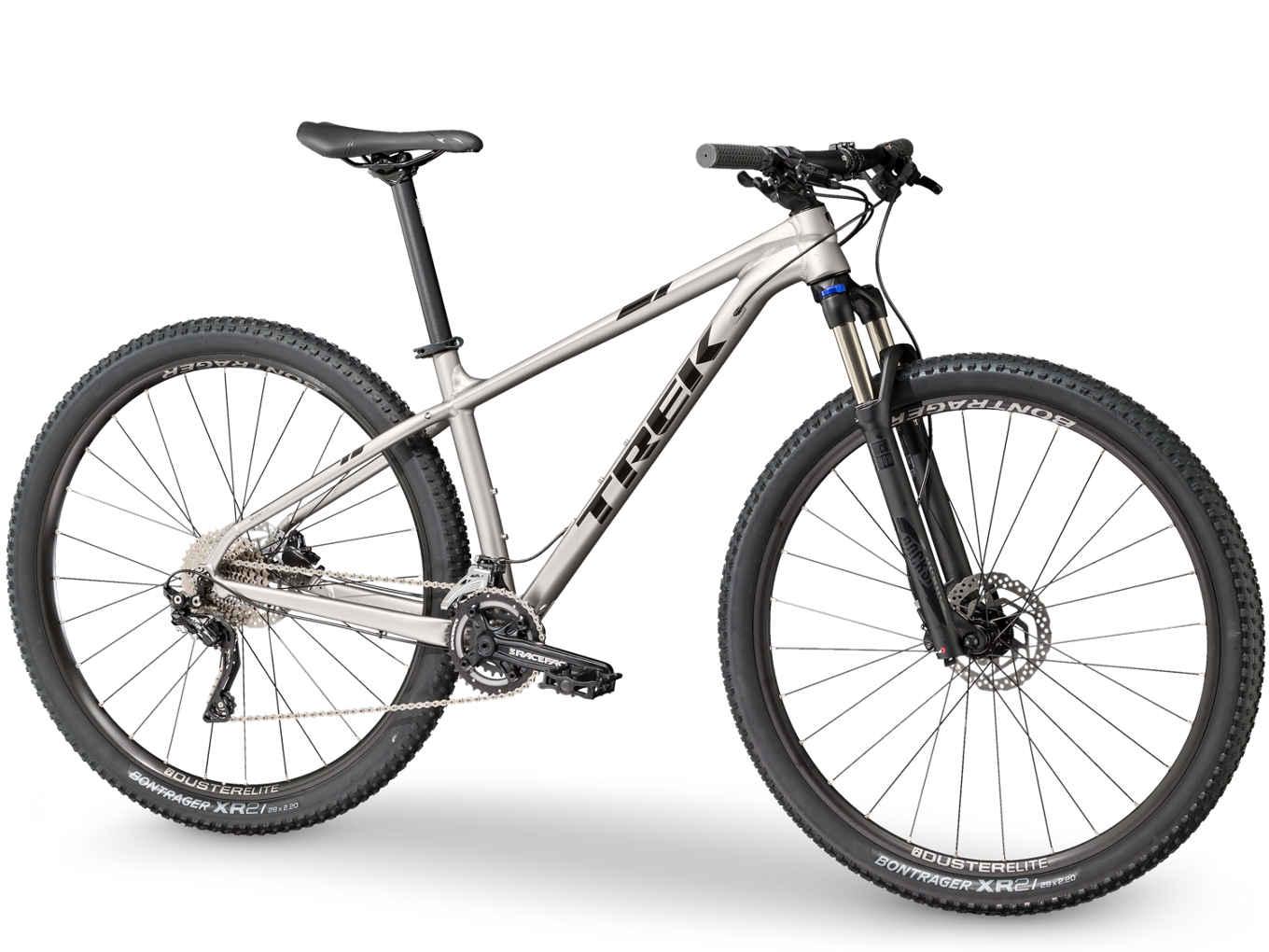 Trek Xcaliber 8: A silver Trek mountain bike with wide tires, showing a front suspension fork, disc brakes, and a modern design suitable for off-road cycling. The bike features a single speed gear system and a lightweight aluminum frame.