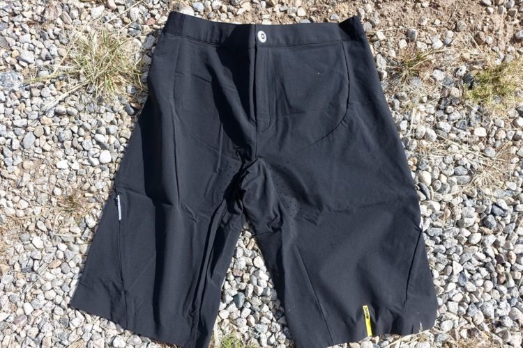 Black shorts laid flat on a gravel surface, featuring a button closure and side pockets. The fabric appears lightweight and suitable for outdoor activities.