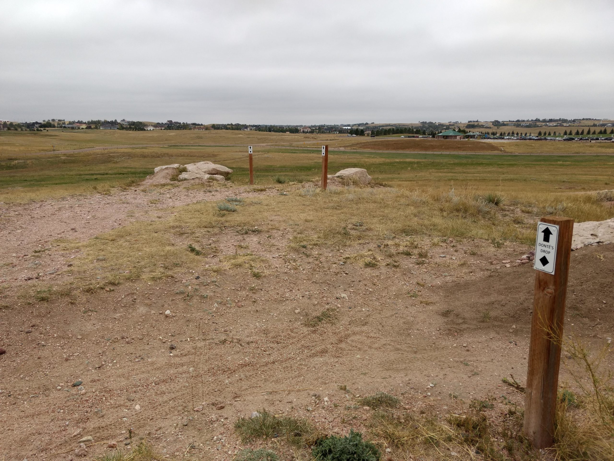 A dirt path in an open grassy area, with several wooden signs indicating different trail directions, including "Donte