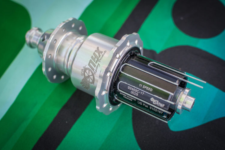 An aluminum bicycle hub featuring an 11-speed configuration, with a polished surface and engraved branding. The hub is positioned on a patterned green and black surface, highlighting its design and technical details.