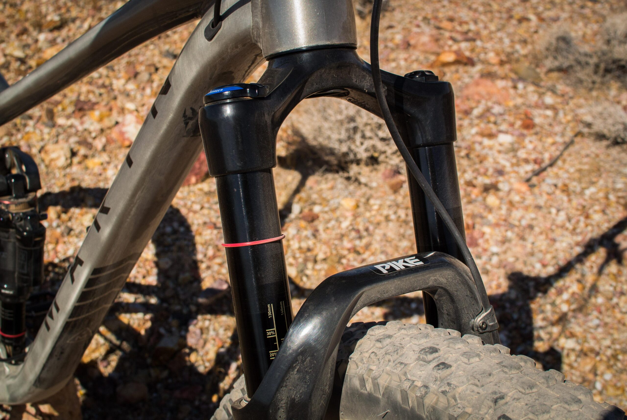 Marin B-17 3: Close-up view of a mountain bike's front suspension fork, showcasing the black Pike model with visible travel adjustments and a textured tire on rugged, rocky terrain.