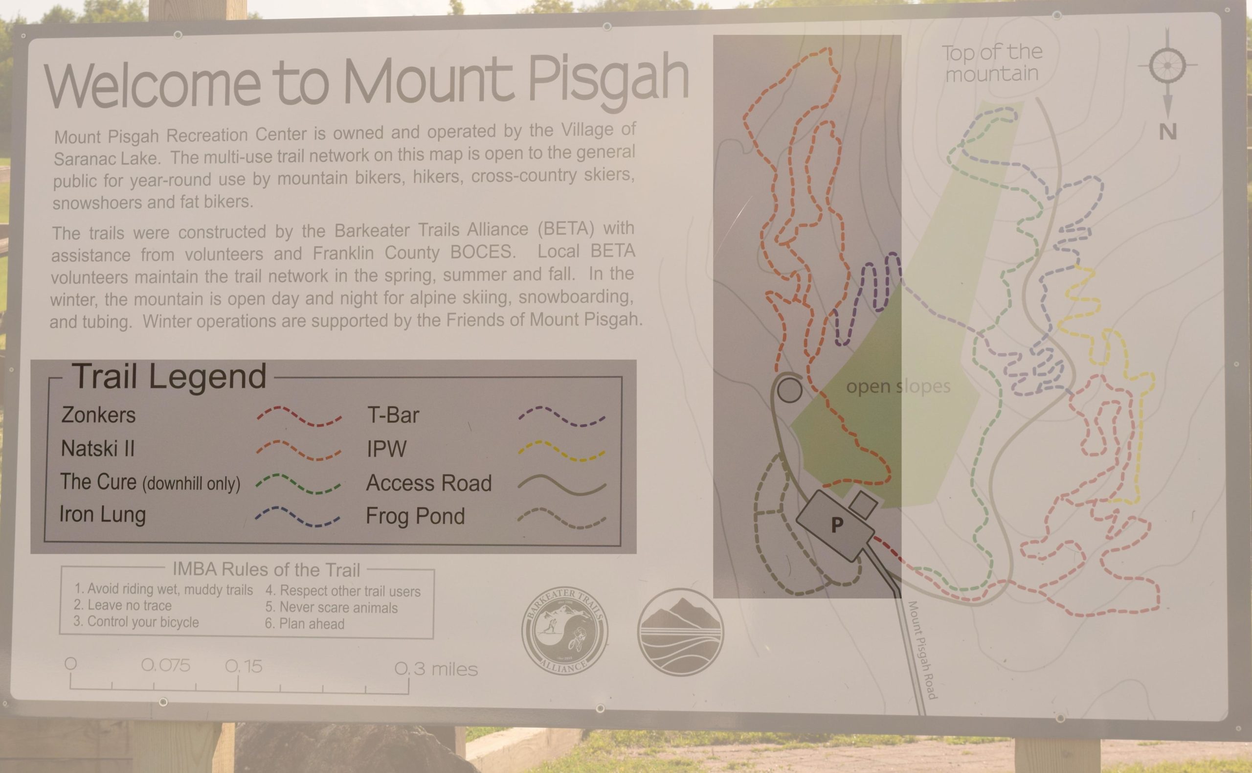 A welcome sign for Mount Pisgah Recreation Center, which includes information about trail accessibility for mountain bikers, hikers, skiers, and snowshoers. The sign features a trail map with different routes illustrated in various colors, along with a legend indicating trail names and types. It highlights the center's operations and maintenance by local volunteers and organizations. Mount Pisgah II: the left side mountain bike trail.