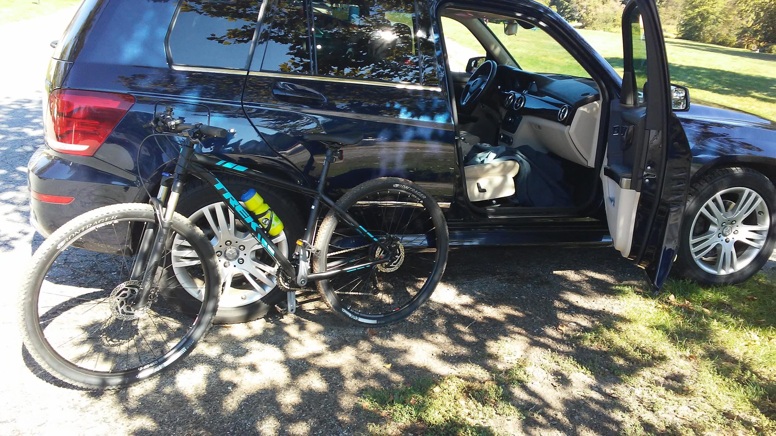 A parked black SUV with an open passenger door, next to a black mountain bike. The bike features blue and yellow accents and is leaning against the vehicle