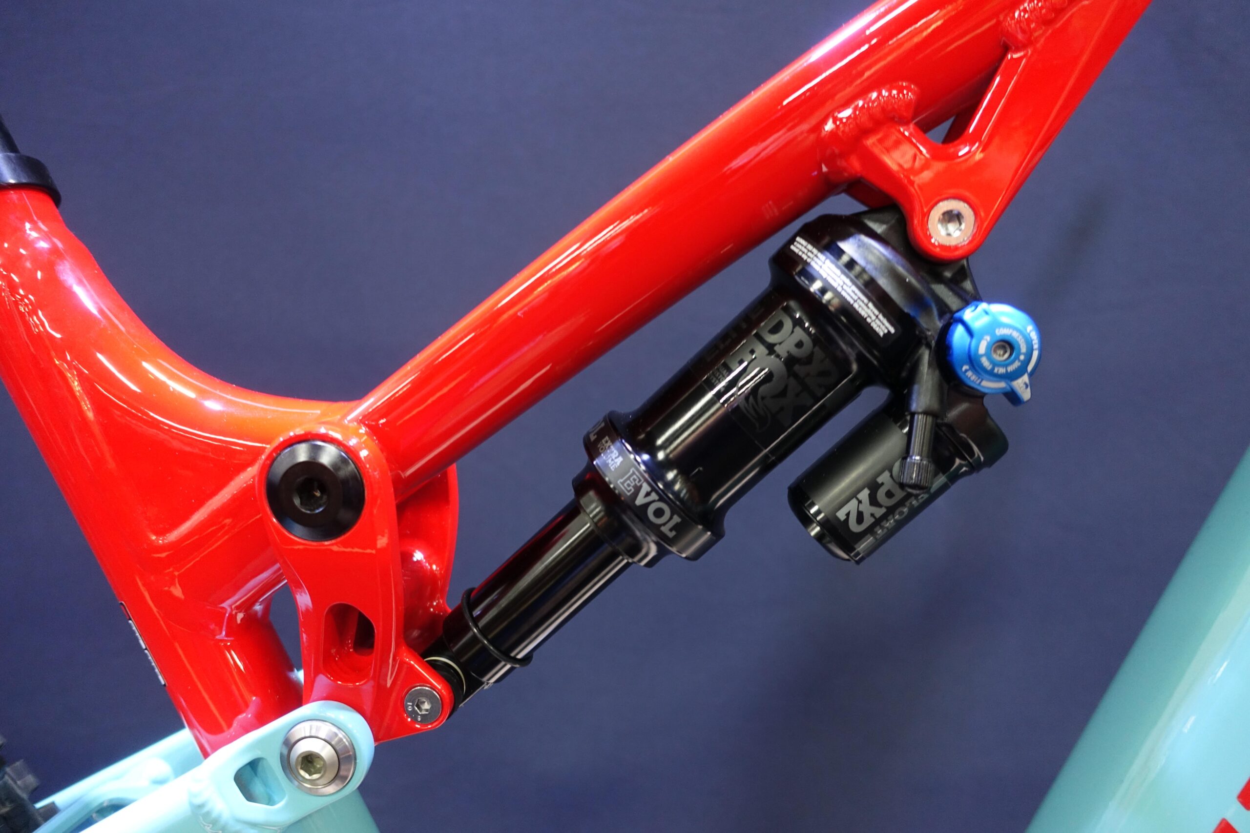Patrol 591: Close-up of a bicycle frame featuring a bright red suspension linkage and a black rear shock absorber, showcasing detailed components and a sleek design against a dark background.