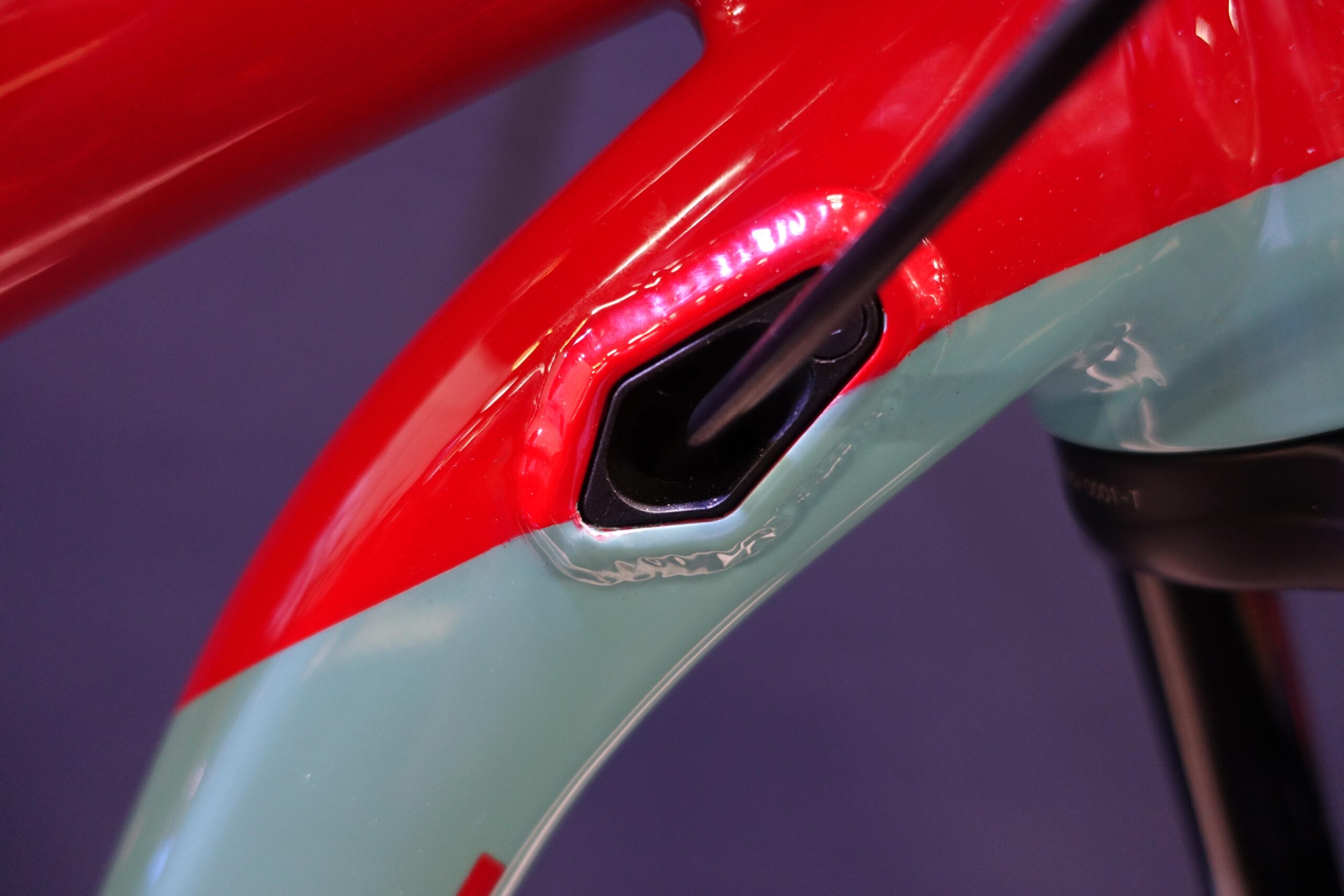 Patrol 591: Close-up image of a bicycle frame featuring a combination of red and teal paint, highlighting a cable entry point on the frame. The background is a solid dark color, enhancing the focus on the frame details.