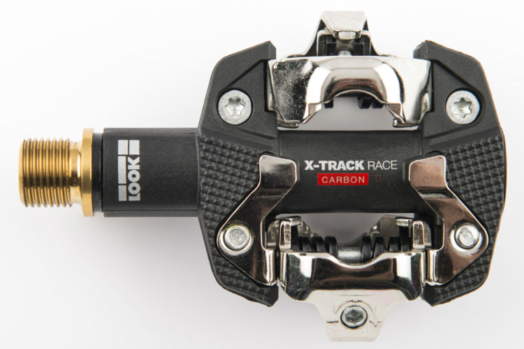 Alt text: "Close-up of a black and silver X-Track Race Carbon bicycle pedal with a gold threaded connector, showcasing the detailed design and mechanism."