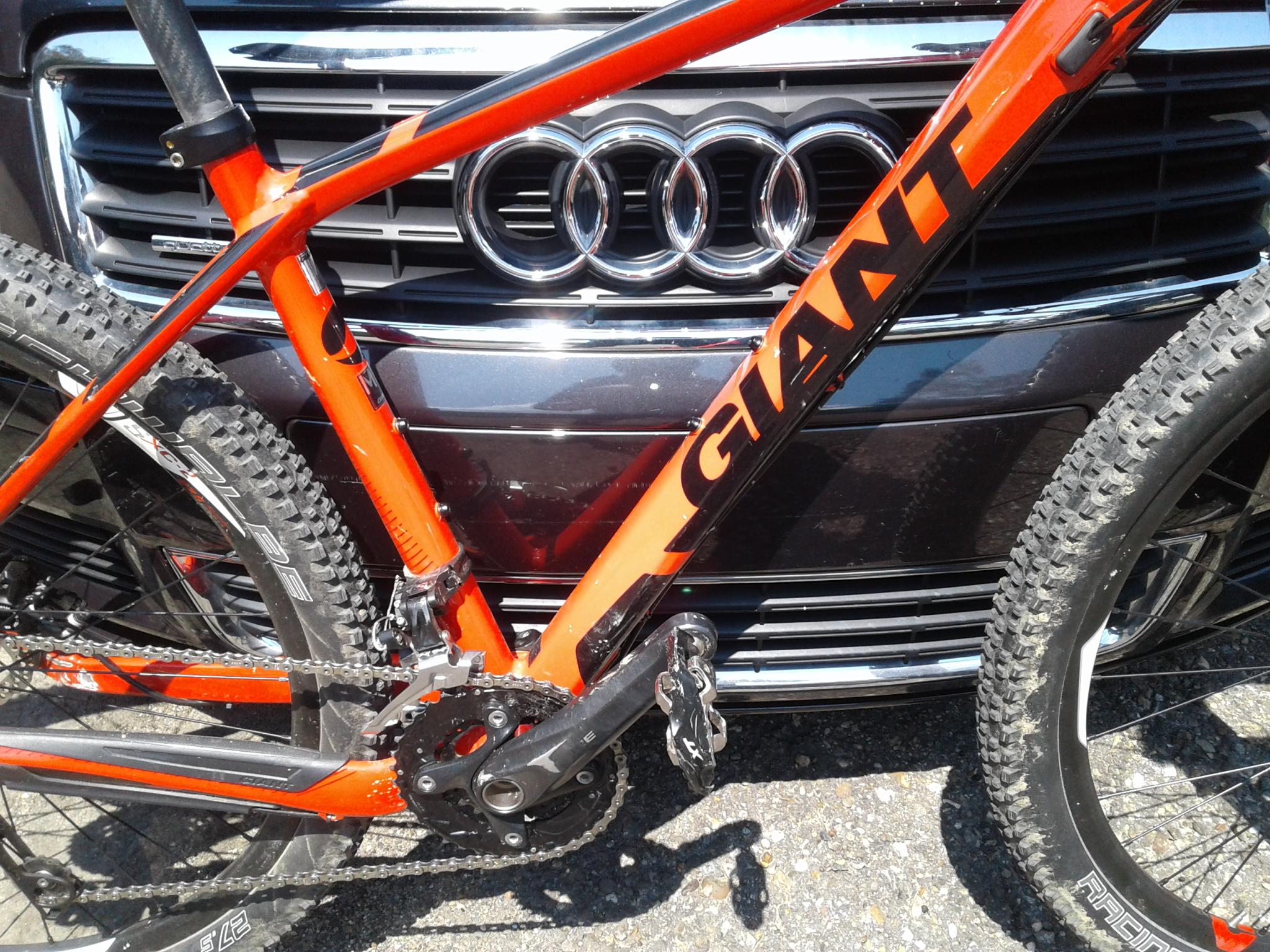 Giant XTC 27.5 2: An orange Giant mountain bike positioned in front of a black Audi car grille. The bike's frame, gears, and wheels are clearly visible, highlighting its design and features.