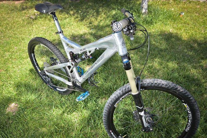 Intense tracer: A silver and black mountain bike positioned on green grass, featuring prominent tires, a front suspension, and colorful pedals. The bike has a modern frame design with various handlebar components visible.