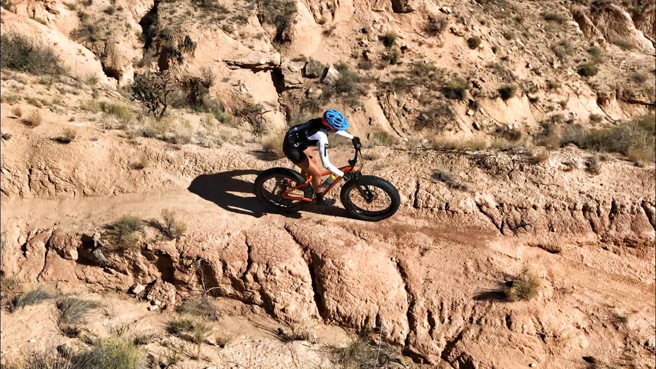 A cyclist navigating a rocky trail on a fat bike, surrounded by rugged terrain and dry vegetation in a sunlit landscape. Mariposa Fat Bike Trails mountain bike trail.