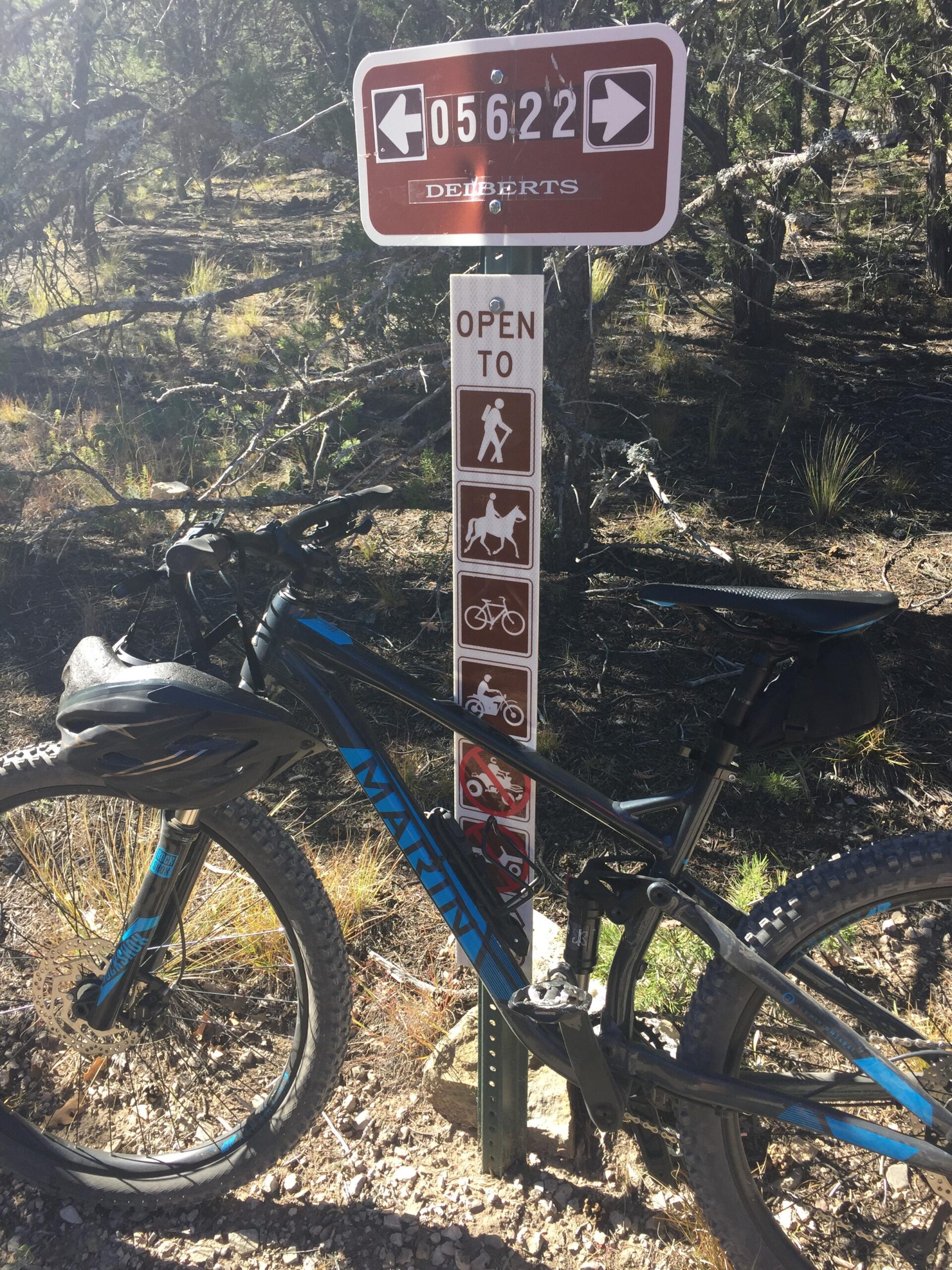 Marin Hawk Hill: A mountain bike is leaning against a trail sign in a forested area. The sign displays the trail number "05622" and indicates that the trail is open to hikers, horseback riders, and cyclists. The surrounding terrain features trees and grass.