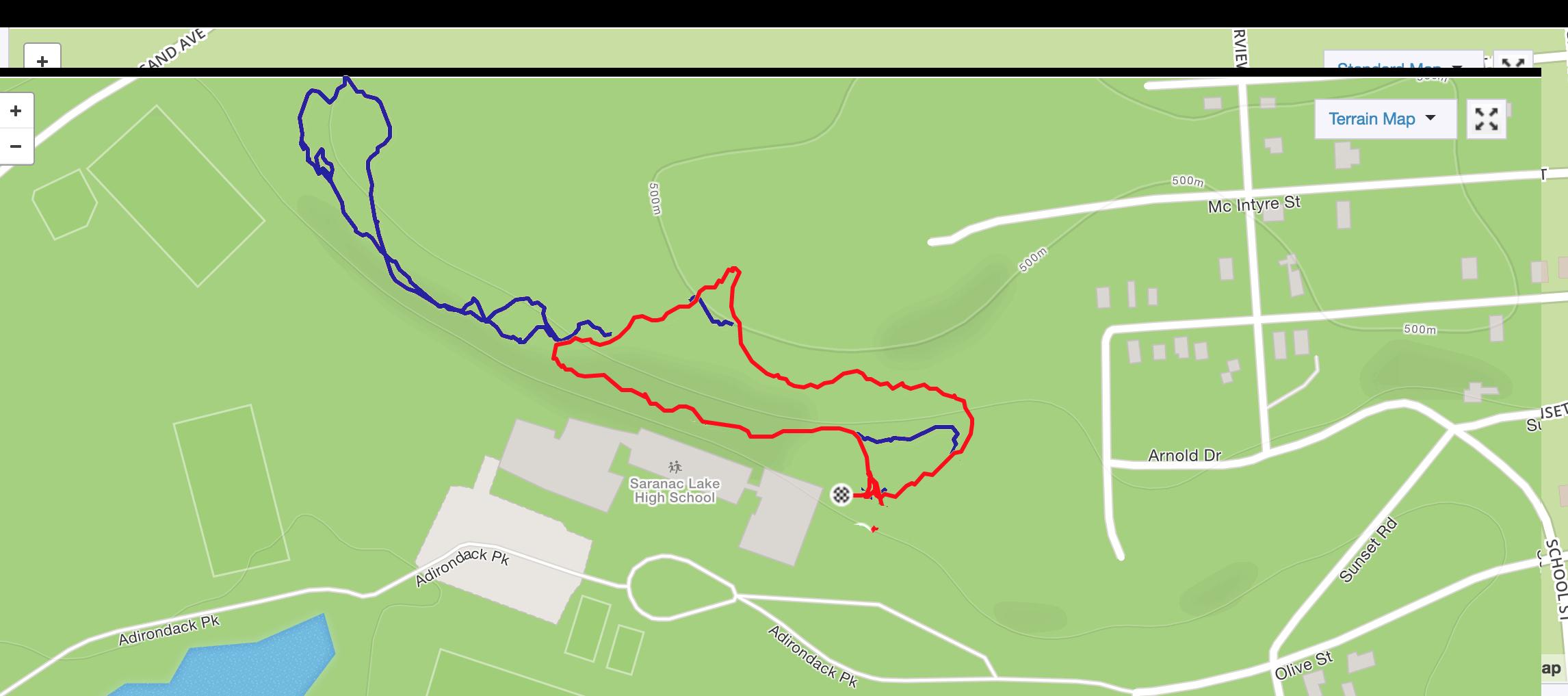A map showing two distinct trail routes represented in blue and red, located in the vicinity of Saranac Lake High School. The area is predominantly green with a lake visible at the bottom left. The map includes street names and a scale indicating distances of 500 meters. Saranac Lake Central School Trail 1 mountain bike trail.