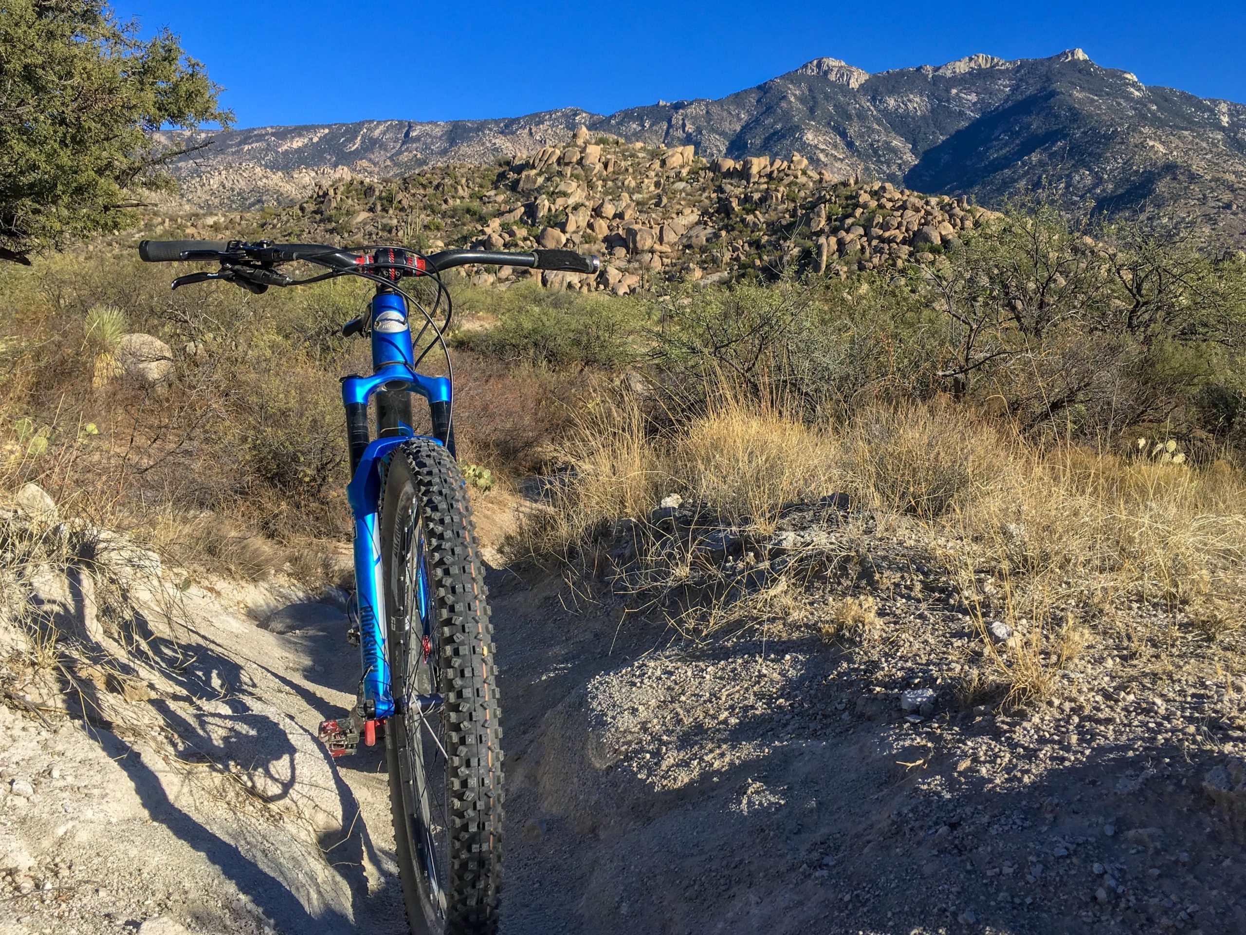A mountain bike on a dirt trail, with rocky hills and blue sky in the background, capturing the essence of outdoor adventure and rugged terrain. 50-year Trail / Golder Ranch mountain bike trail.