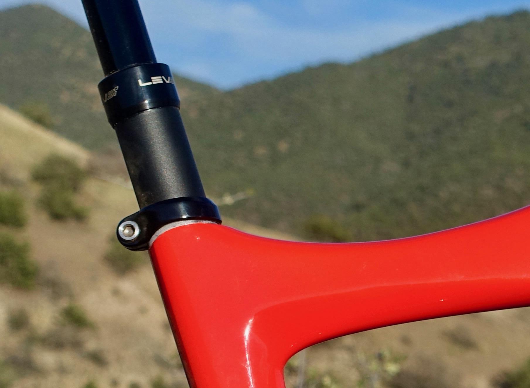 Ibis Mojo HD4: Close-up of a red bike frame featuring a black seat post and a lever mechanism, set against a blurred background of rolling hills and greenery.