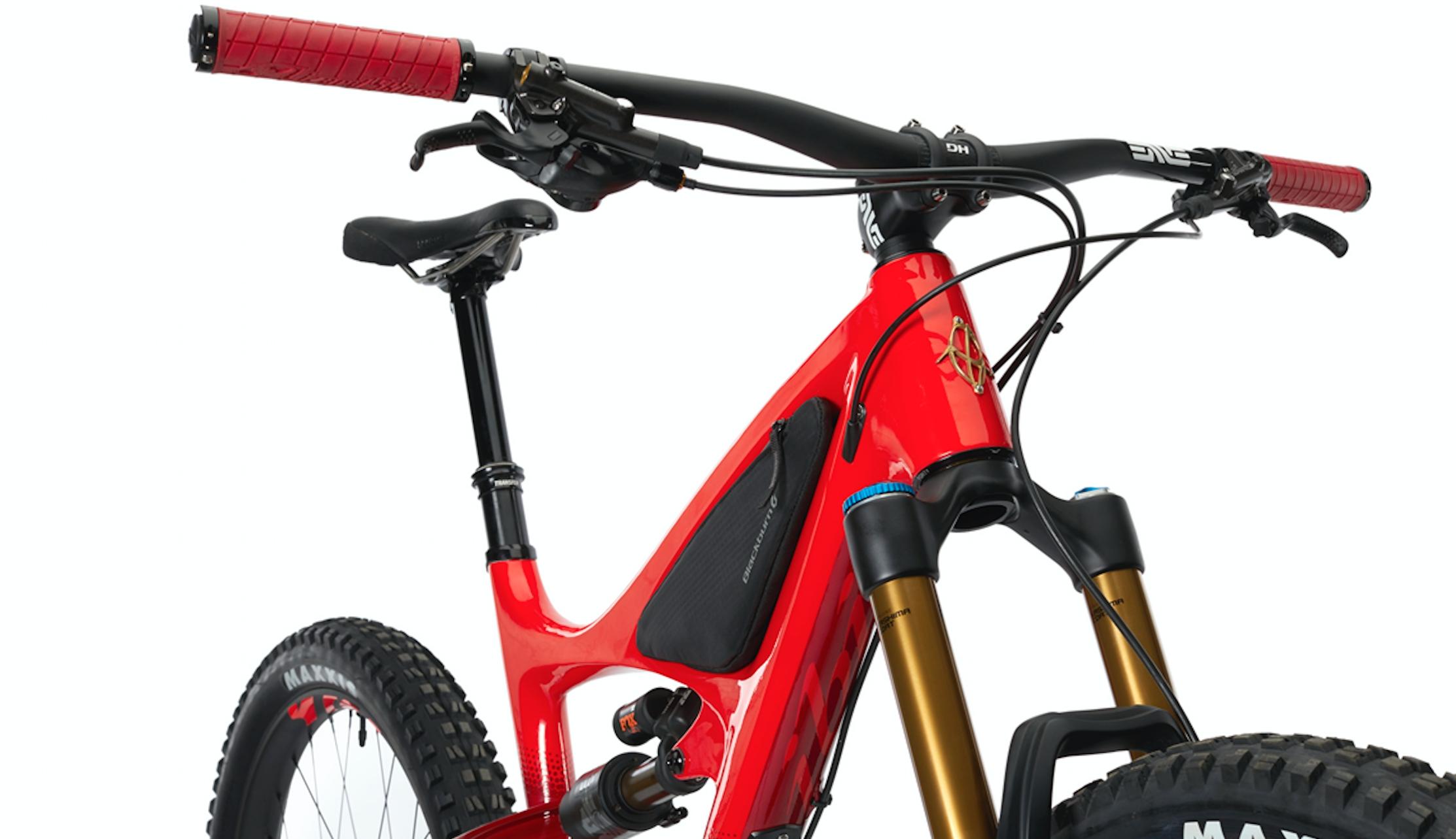 Ibis Mojo HD4: A close-up view of a red mountain bike featuring a sleek frame design, adjustable handlebars with red grips, and a prominent front shock absorber. The bike displays a black storage pouch on the frame, and the tire has a rugged tread pattern, indicating its suitability for off-road use.
