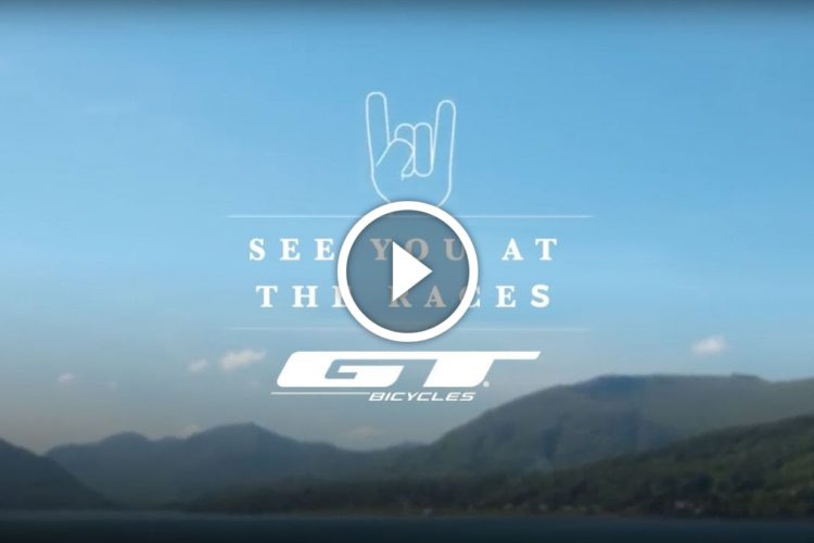 A serene landscape featuring mountains and a clear blue sky, overlaid with the text "SEE YOU AT THE RACES" and the GT Bicycles logo. A play button indicates that the image is part of a video.