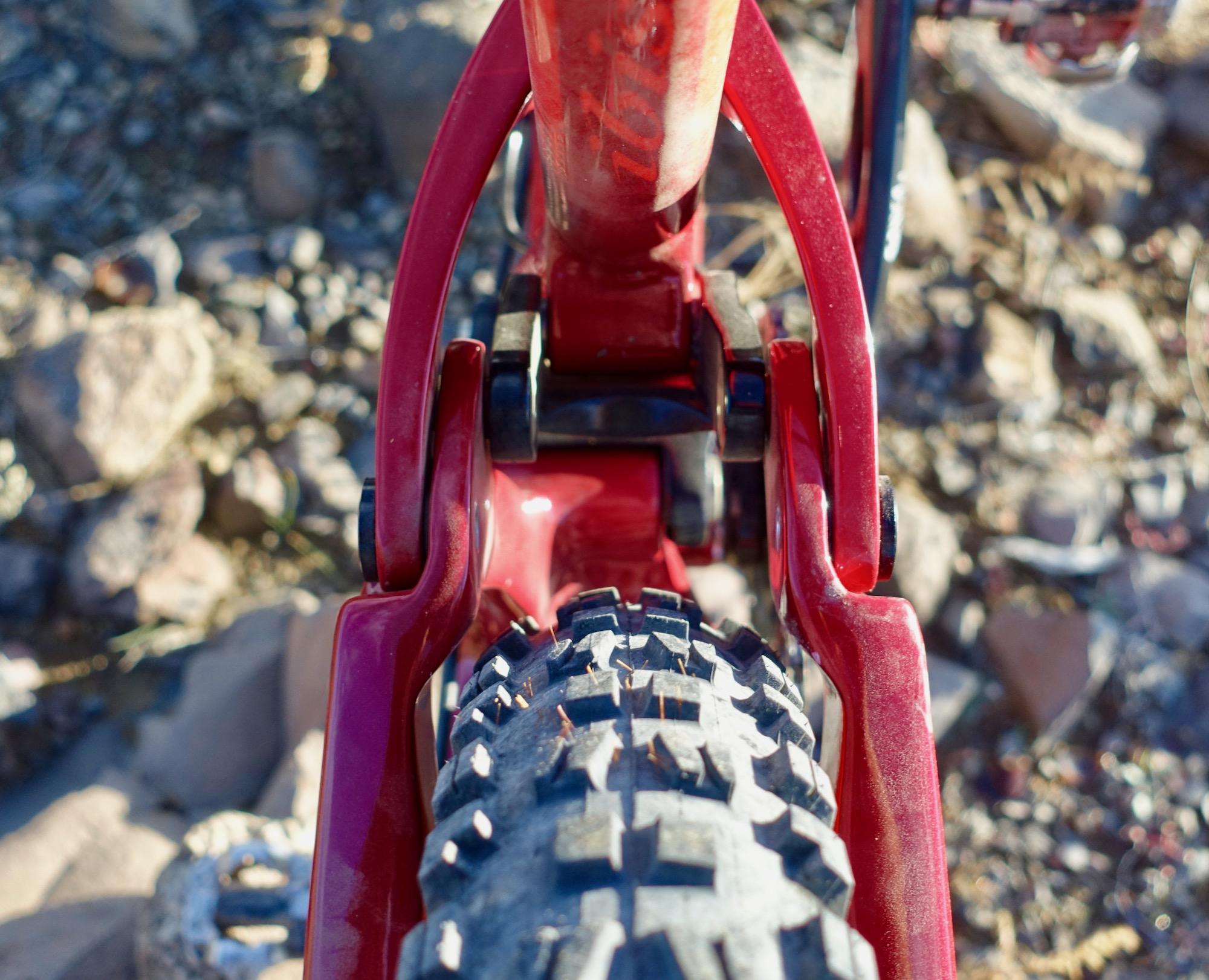 Ibis Mojo HD4: Close-up view of a red bicycle's rear tire and suspension system, showcasing the intricacies of the frame and tire tread against a rocky surface.