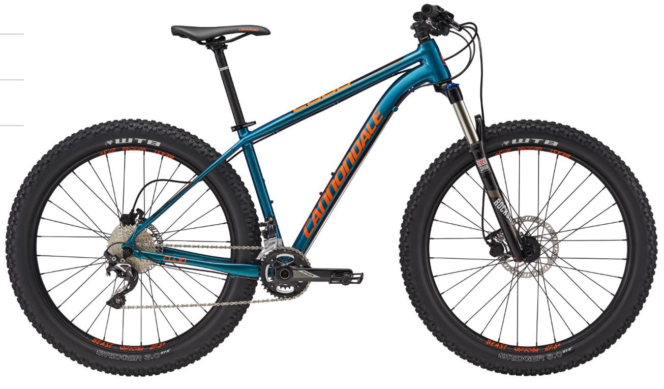 Cannondale Cujo 2: A blue and orange mountain bike with wide tires and a sturdy frame. The bike features a front suspension fork and is equipped with a Shimano drivetrain. The wheels are marked with WTB branding, indicating their designed use for off-road terrain. The bike is showcased against a plain background, highlighting its design and features.
