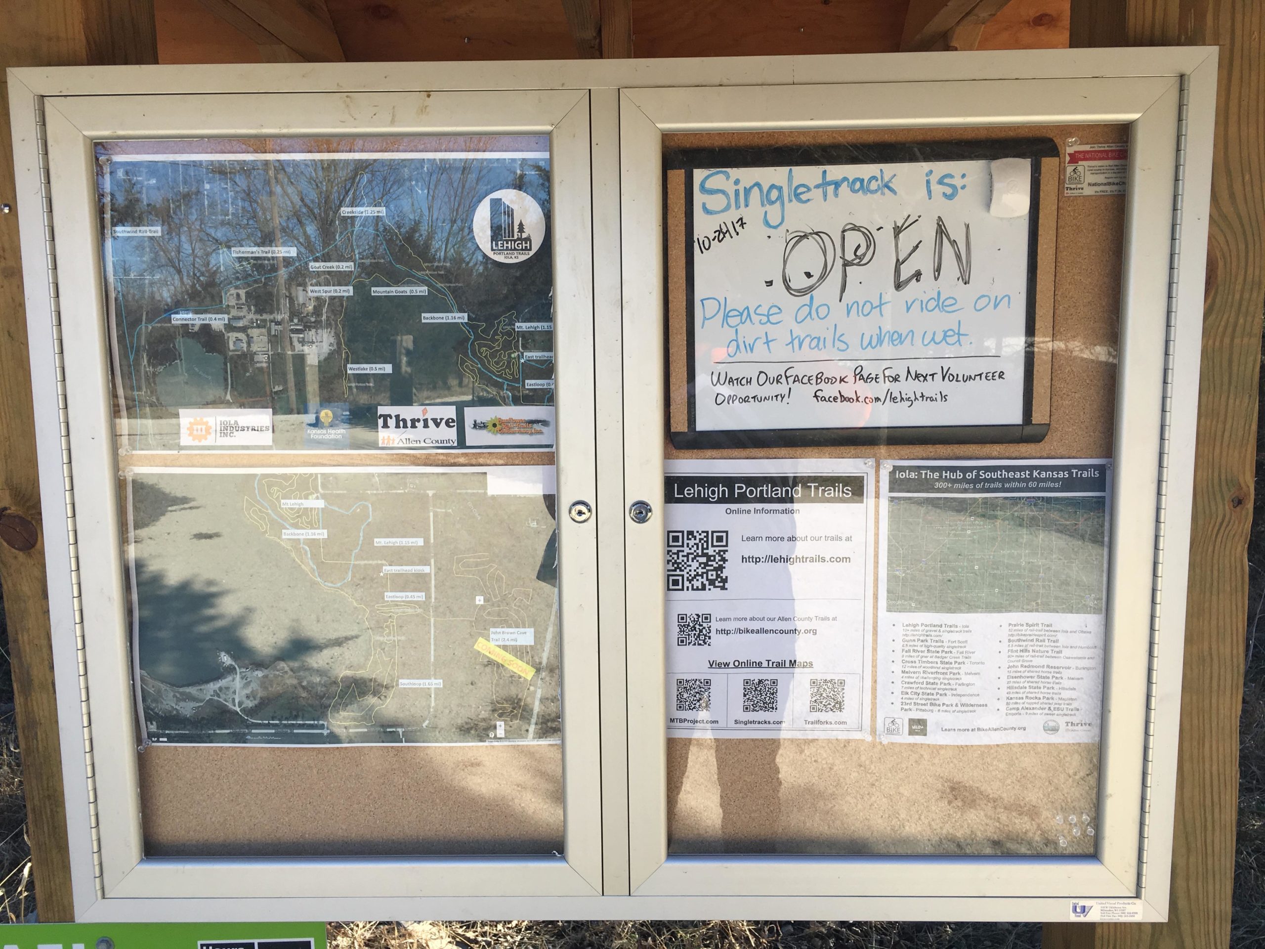 Information board displaying maps and trail guidelines. A sign indicates that the singletrack trails are open, alongside a warning not to ride on dirt trails when wet. The board includes QR codes for online trail maps and social media links for volunteer opportunities in Lehigh Portland Trails. Lehigh Portland Trails mountain bike trail.