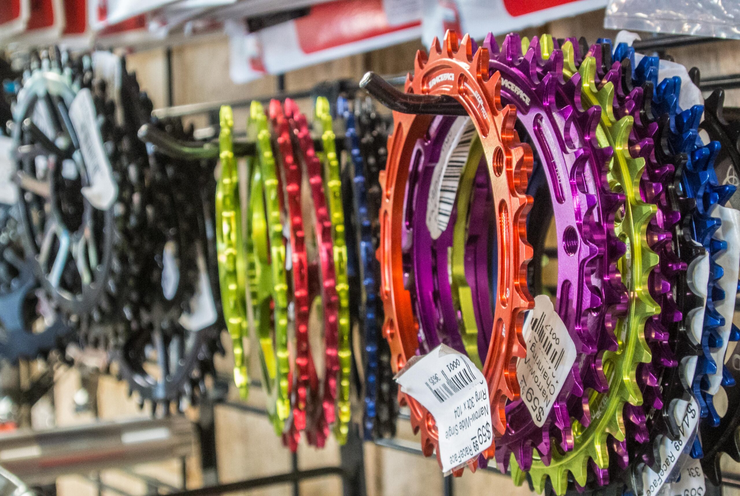 A display of colorful bicycle chainrings hanging on a rack, featuring various colors such as black, green, red, orange, purple, and blue, each tagged with price labels.