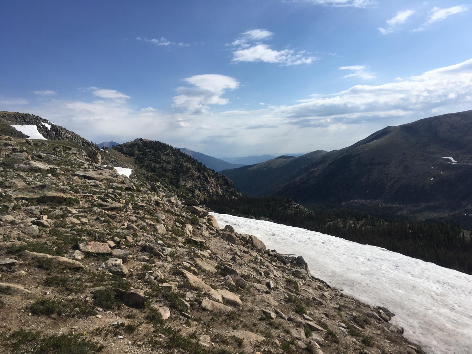 Scenic mountain landscape featuring rocky terrain, patches of snow, and rolling hills under a partly cloudy sky. Monarch Crest Trail mountain bike trail.