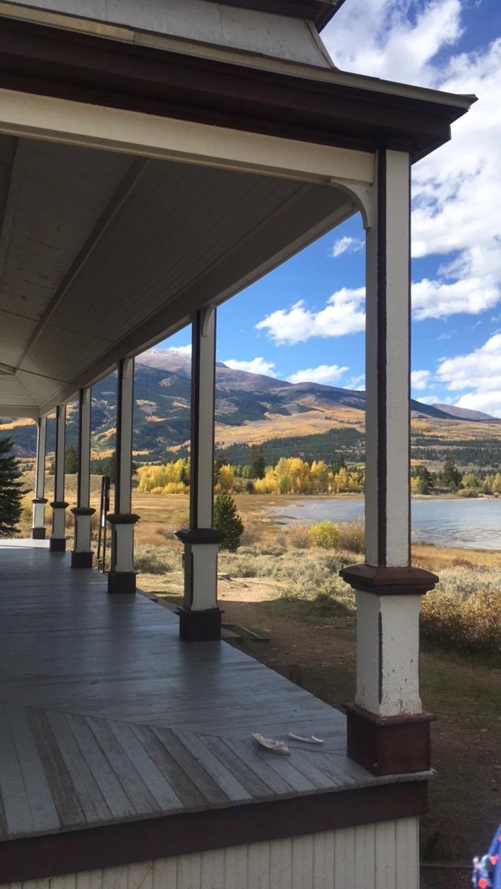 A view from a wooden porch overlooking a serene landscape with mountains in the background, colorful autumn foliage, and a calm body of water. The sky is partially cloudy, adding to the scenic beauty of the setting. Twin Lakes Loop mountain bike trail.