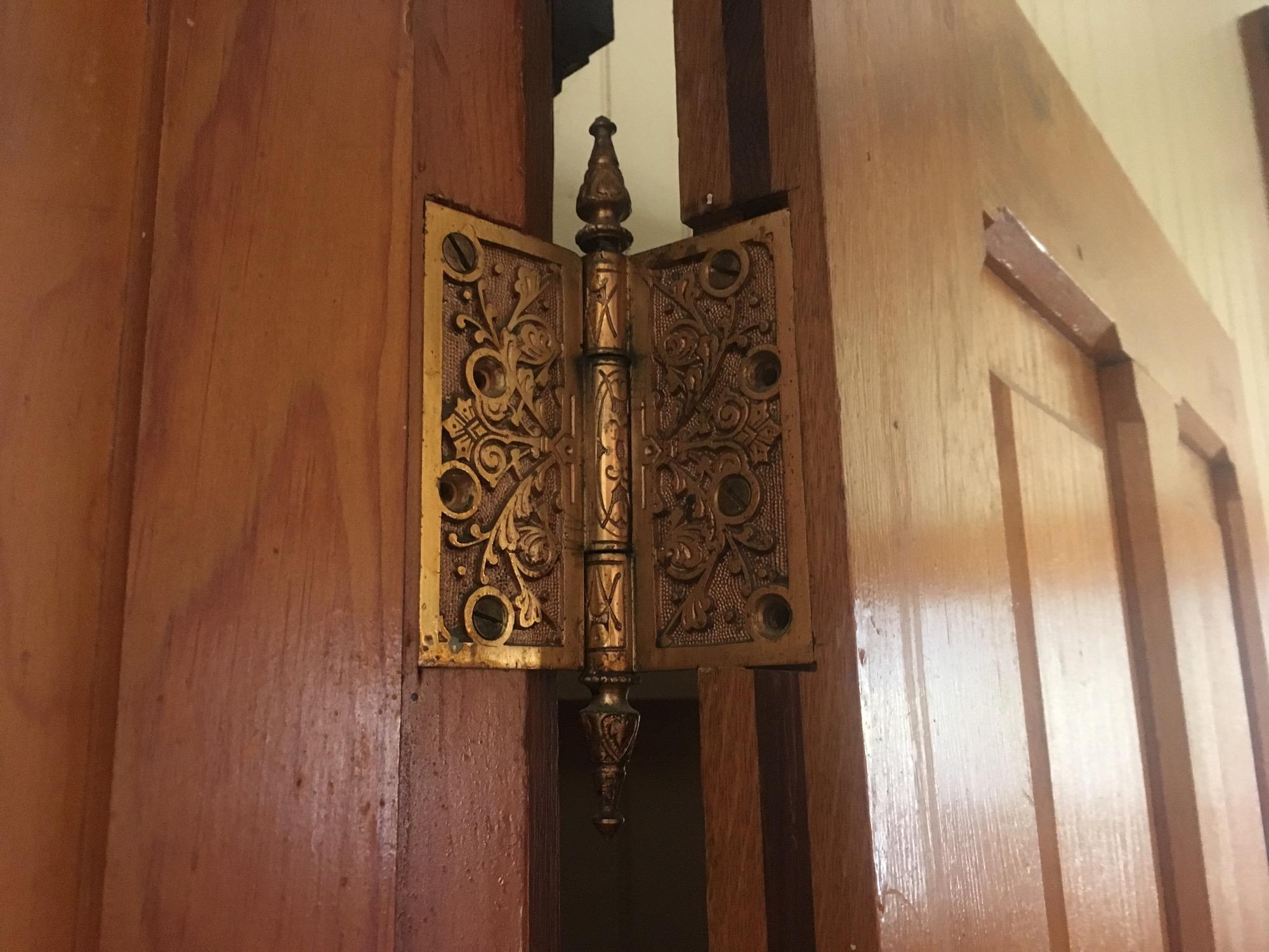 Close-up image of an ornate door hinge with intricate designs, mounted on a wooden door. The hinge features a decorative pattern, highlighted by a gold finish, contrasting with the natural wood grain of the door. Colorado Trail: Clear Creek Thd to Lake View CG / Hwy 82 mountain bike trail.