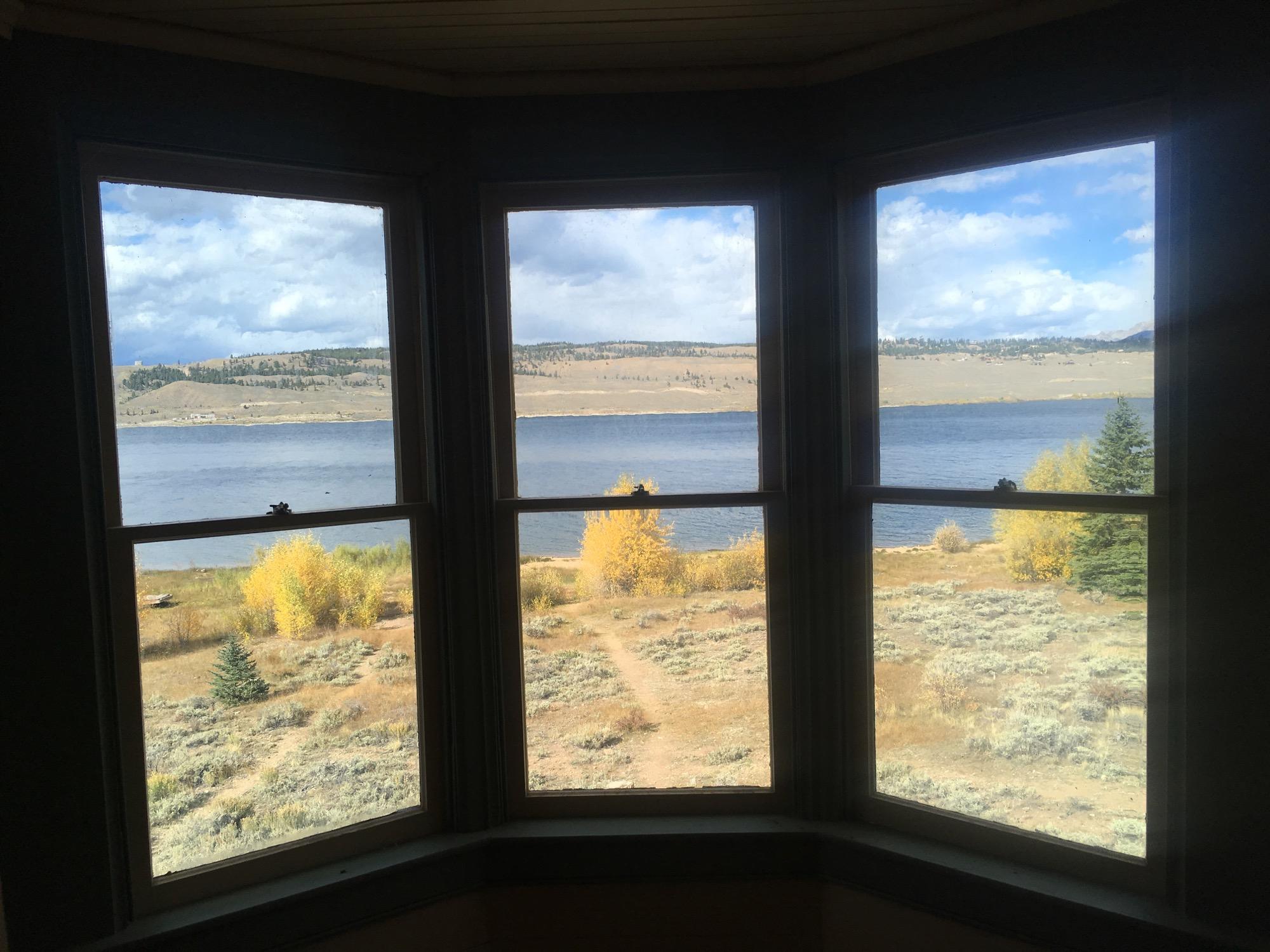 Scenic view through three windows overlooking a calm lake surrounded by autumn foliage, with hills in the background under a partly cloudy sky. Twin Lakes Loop mountain bike trail.