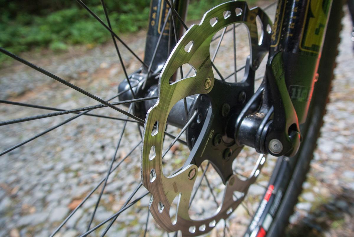 Niner Air 9 RDO: Close-up view of a bike's disc brake, showcasing the metallic brake rotor and surrounding spokes against a rocky surface background.