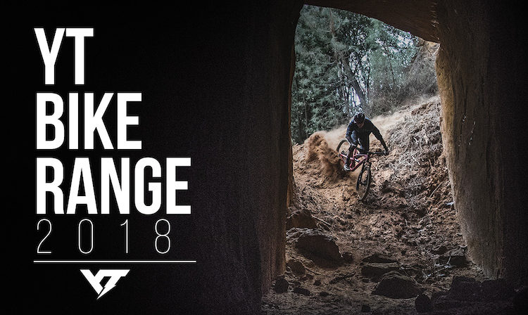 A mountain biker navigating a rugged trail through a rocky tunnel, kicking up dust as they ride with energy and skill. The image features the text "YT Bike Range 2018" prominently displayed on the left side.
