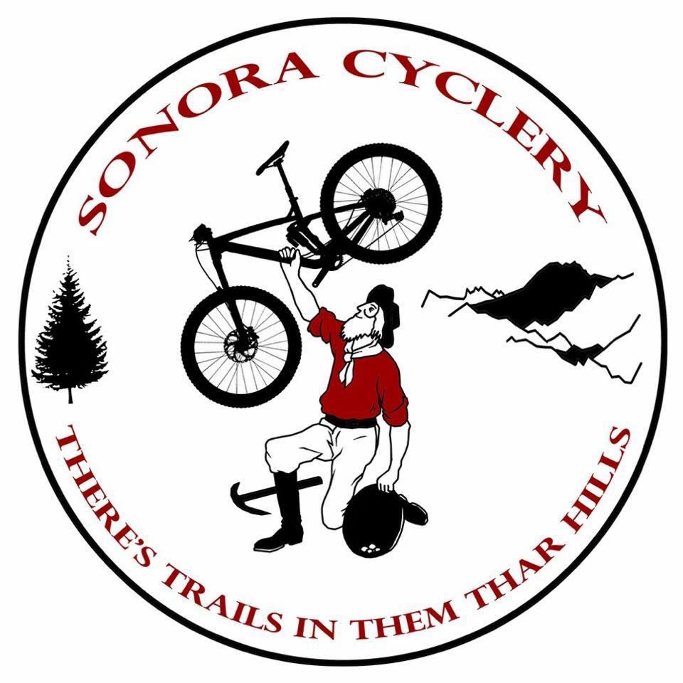 A circular logo featuring a person in historical attire, lifting a mountain bike above their head. To the left, there is a stylized evergreen tree, and in the background, a range of mountains is depicted. The text "SONORA CYCLERY" is written at the top in red, while the phrase "THERE'S TRAILS IN THEM THAR HILLS" curves along the bottom. The overall design combines elements of outdoor adventure with a whimsical, rustic theme.