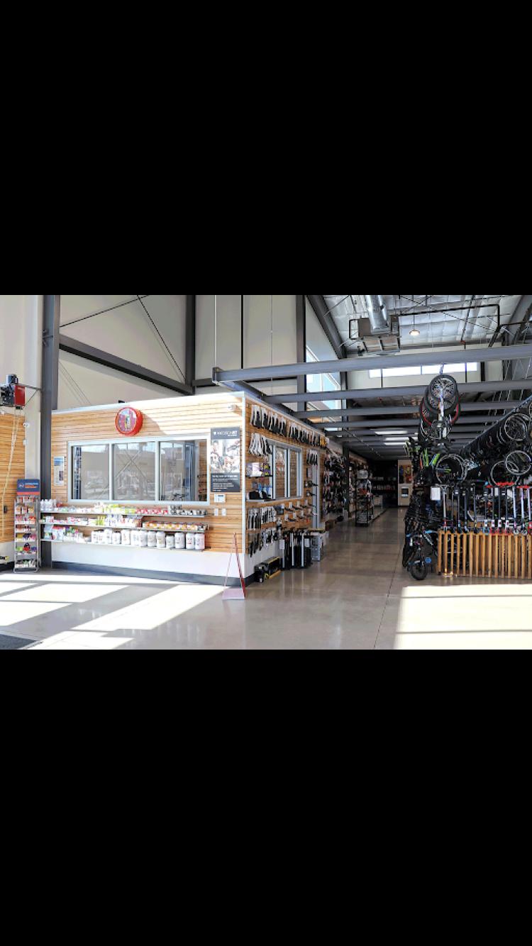 Interior view of a sporting goods store featuring a display area for various equipment. On the left, there is a wooden counter with merchandise and informational signage, while the right side showcases bicycles and other sporting gear lined up along the wall. The space is well-lit with large windows, providing a bright and open atmosphere.