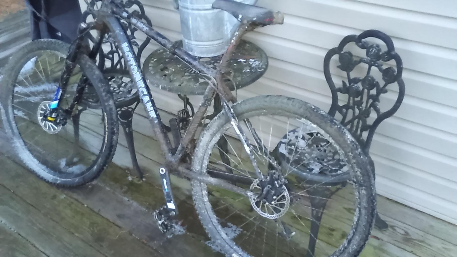 Motobecane Motobecane 529 HT: A muddy mountain bike leaned against a decorative metal table and chair on a wooden deck, with a bucket visible in the background.