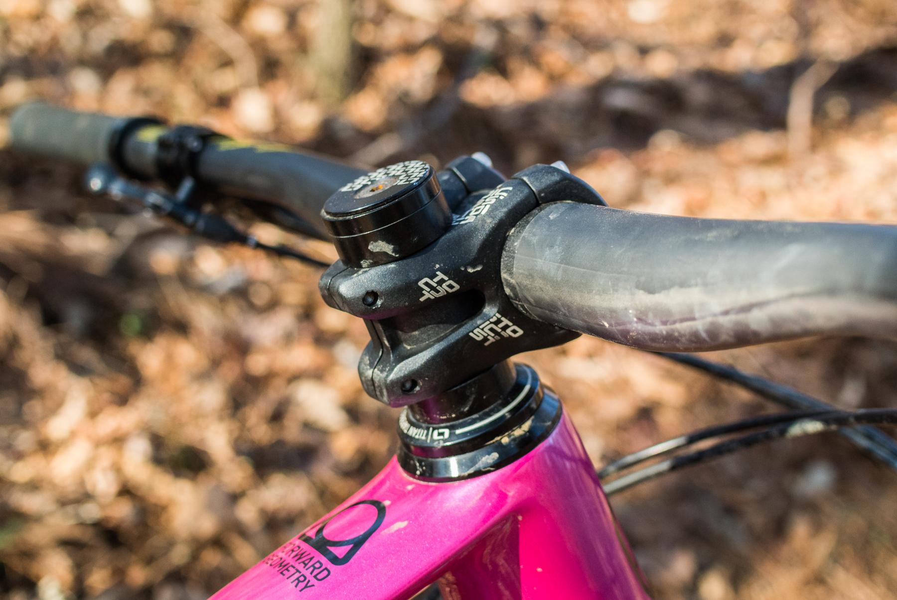 Mondraker Dune: Close-up view of a bicycle's handlebars and stem, featuring a pink frame and black components. The image showcases the bike's design and details, set against a background of autumn leaves.