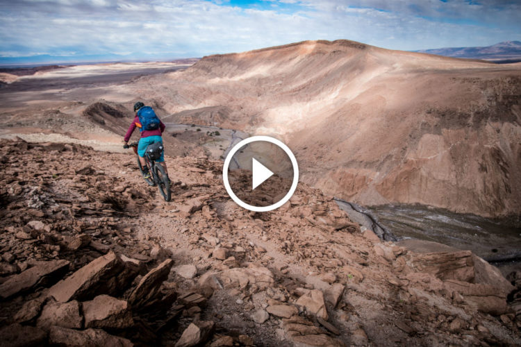 A mountain biker navigates a rocky terrain overlooking a vast canyon landscape under a partly cloudy sky. The scene captures the adventurous spirit of outdoor cycling in a rugged environment.