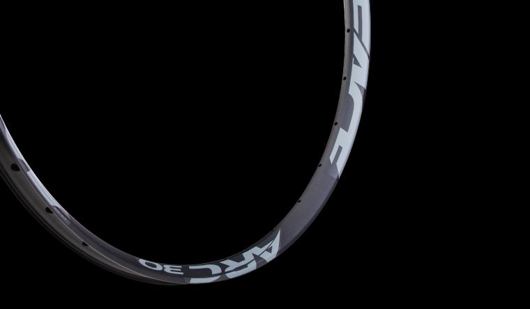 Race Face Arc 30 rim: A close-up image of a bicycle rim with a sleek design, featuring the text "ARC 30" in a bold white font against a dark background. The rim showcases a modern profile, emphasizing its lightweight and durable construction suitable for cycling.
