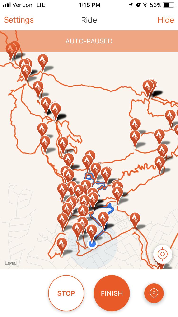A mobile app interface displaying a map marked with various location pins. The screen indicates that the ride feature is auto-paused, and shows options to stop or finish the ride at the bottom. There is a blue path highlighted on the map, suggesting a specific route taken. The map has a light background and features multiple clusters of markers in different areas. Mariposa Fat Bike Trails mountain bike trail.