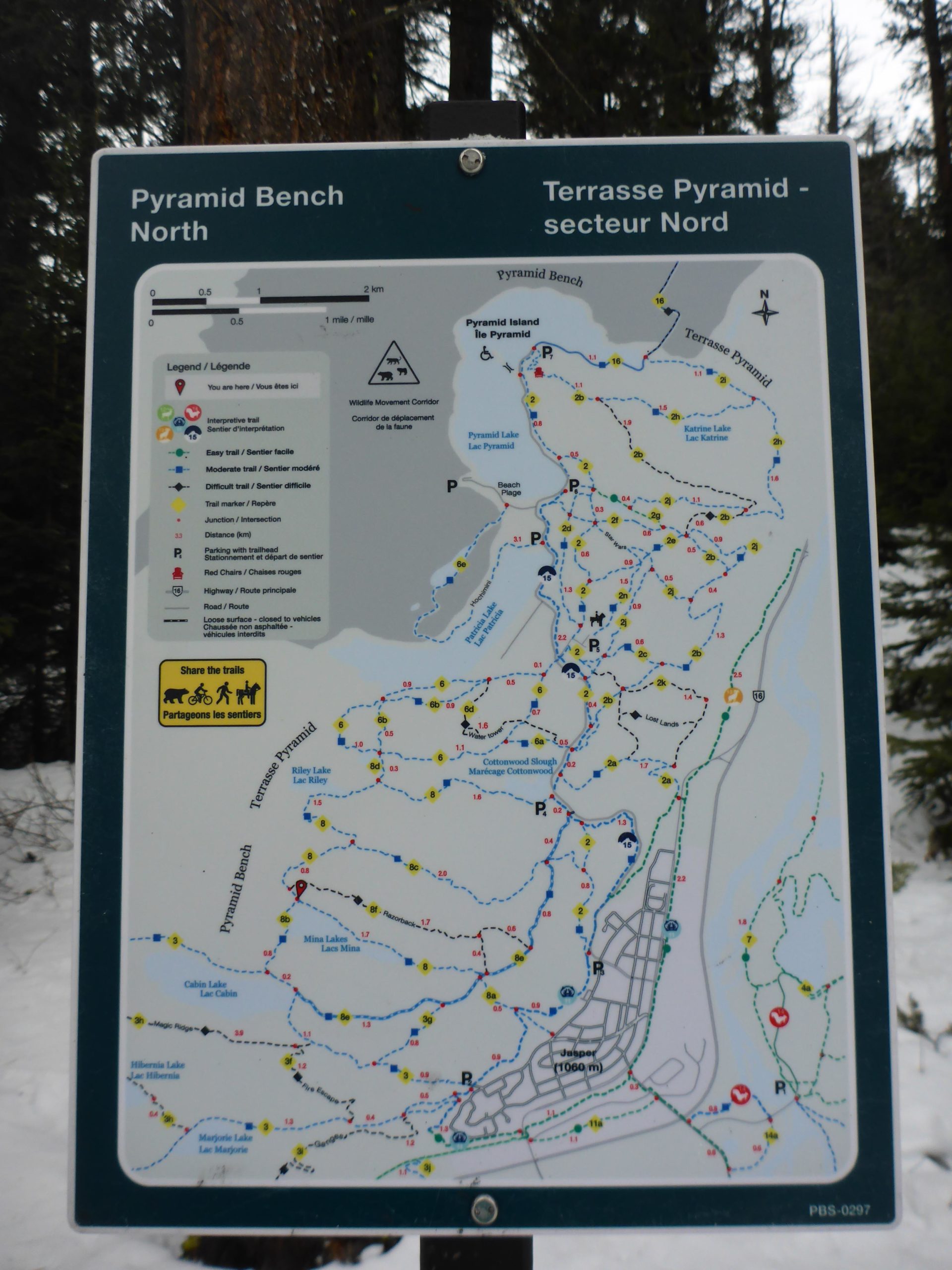 Map of the Pyramid Bench area in Jasper National Park, indicating various trails and distances. The map includes a legend for different trail types, features, and points of interest, with north direction indicated at the top. Surrounding trees and snow can be seen in the background. Pyramid Bench mountain bike trail.