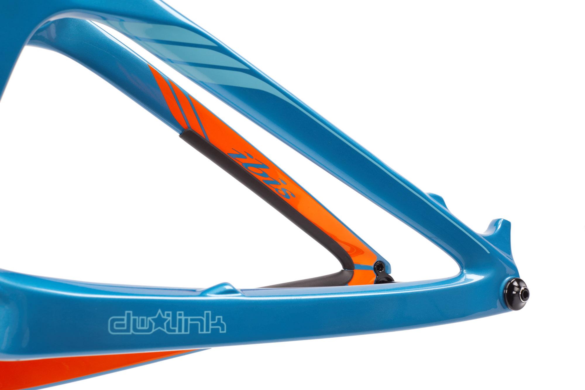 Ibis RipMo: Close-up of a blue bicycle frame featuring orange accents, highlighting the DW link suspension design and a sleek, modern aesthetic. The frame showcases a smooth finish with branding visible on the side.