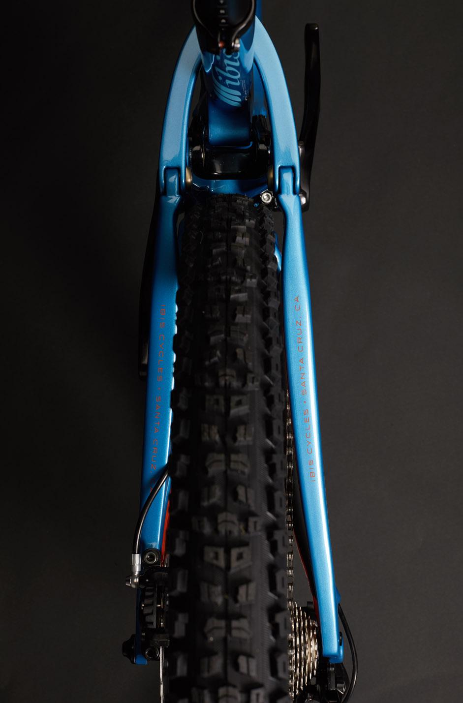 Ibis RipMo: A close-up view of a blue mountain bike frame from a top-down perspective, showcasing the rear wheel and tire tread against a dark background. The bike features prominent branding on the frame, including text identifying the manufacturer, and details of the bike's design elements, such as the suspension setup and gear system.