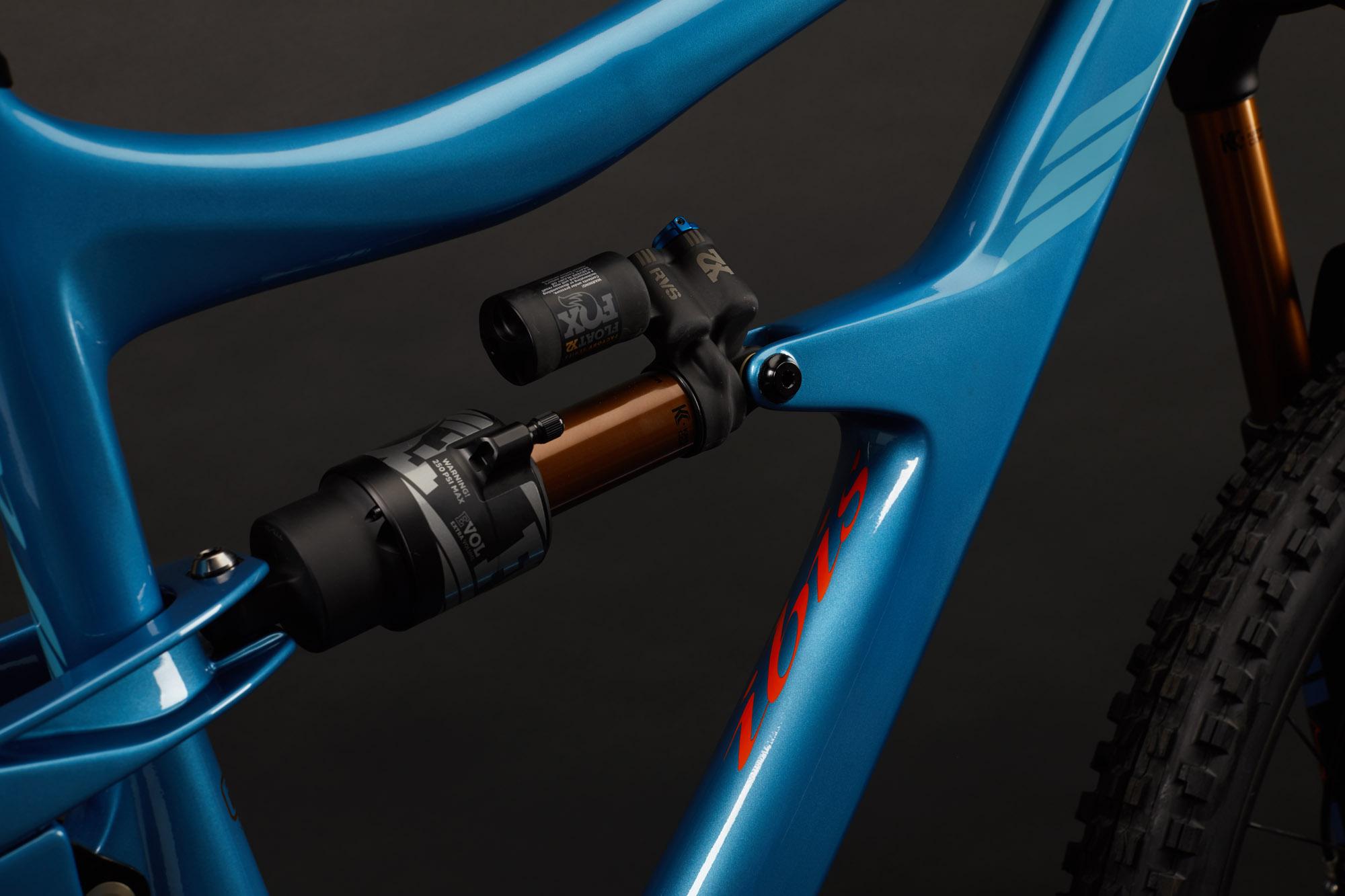 Ibis RipMo: Close-up view of a vibrant blue bicycle frame featuring intricate suspension components, including a black and brown shock absorber and a tuning knob. The background is a smooth dark surface, highlighting the details of the frame and components.