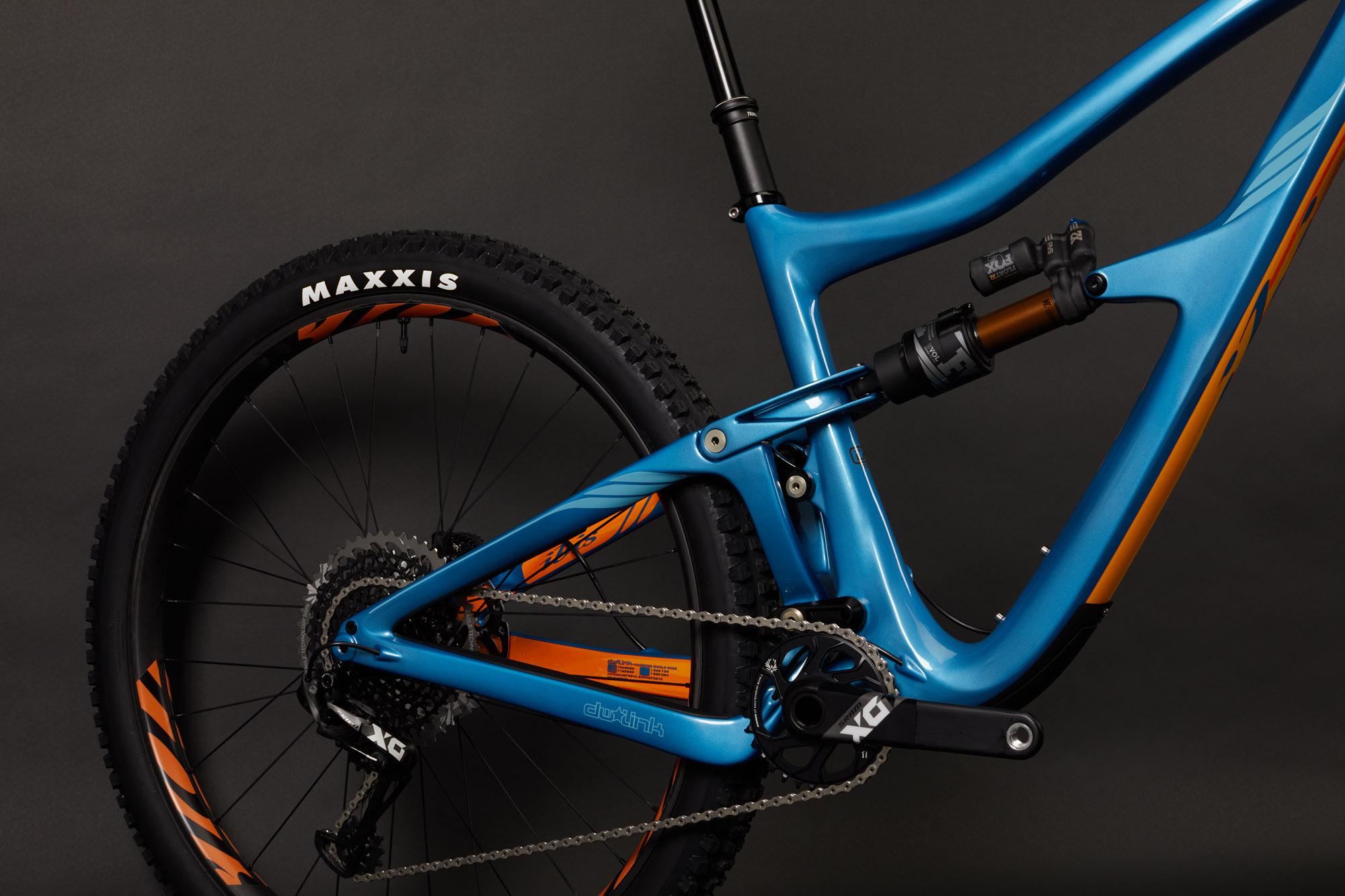 Ibis RipMo: Image of a blue mountain bike featuring a lightweight frame with orange accents. The bike showcases a visible rear suspension system, a Maxxis tire on the back wheel, and a detailed view of the drivetrain, including the derailleur and chain. The background is a solid dark color, emphasizing the bike's vibrant design.