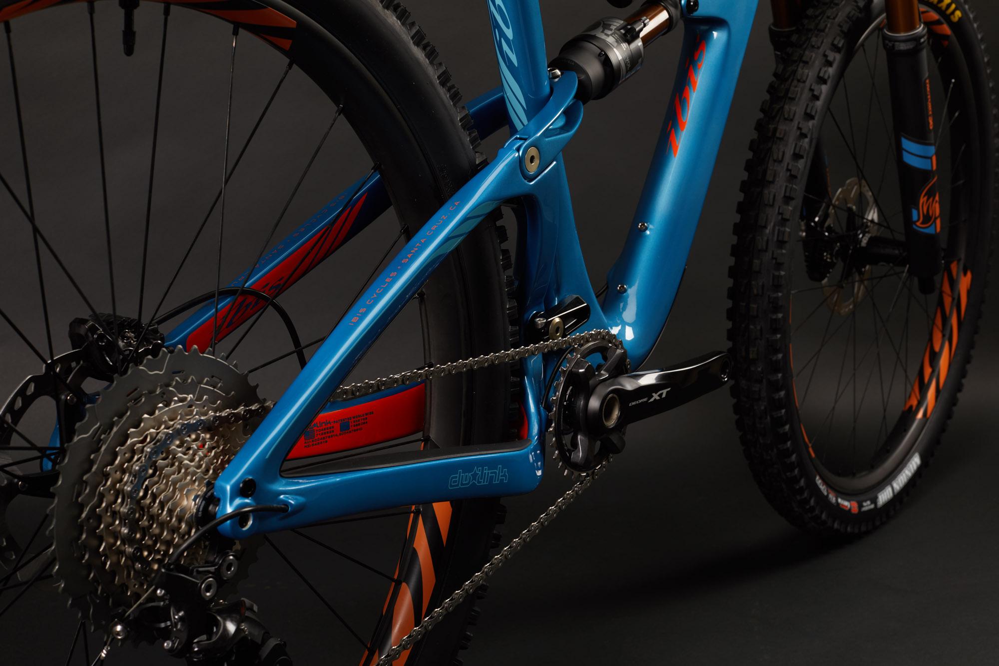 Ibis RipMo: Close-up view of a mountain bike displaying a vibrant blue frame, intricate drivetrain components, and knobby tires. The bike features a black cassette and cranks with silver details, set against a dark background that highlights its design and color contrasts.