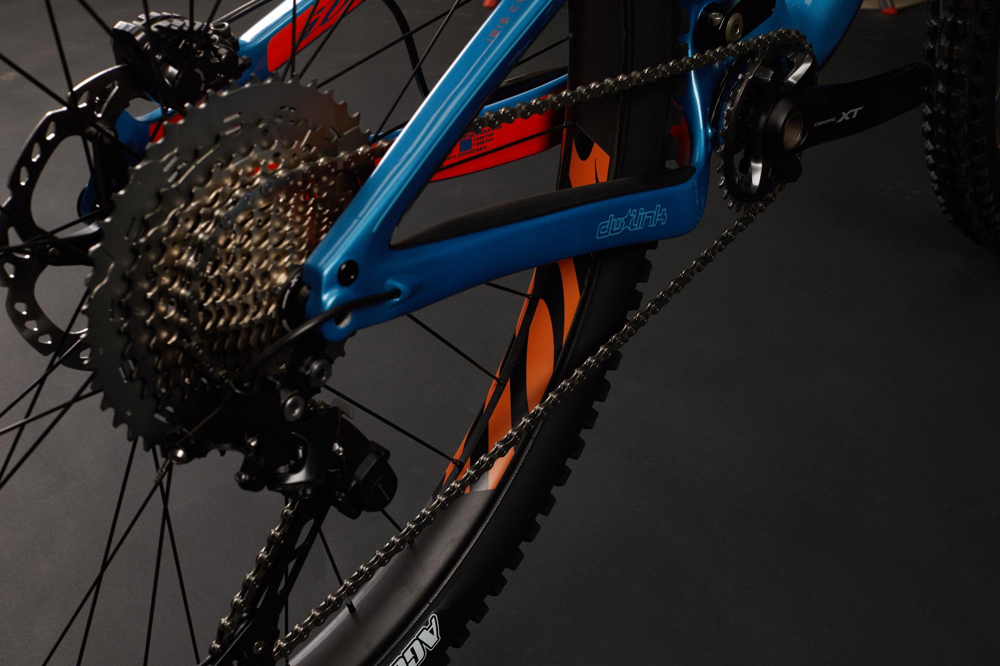 Ibis RipMo: Close-up view of a mountain bike's drivetrain, showcasing a blue frame, a chain, and a geared cassette. The image captures details of the rear wheel, including the tire tread and rim design, against a dark background.