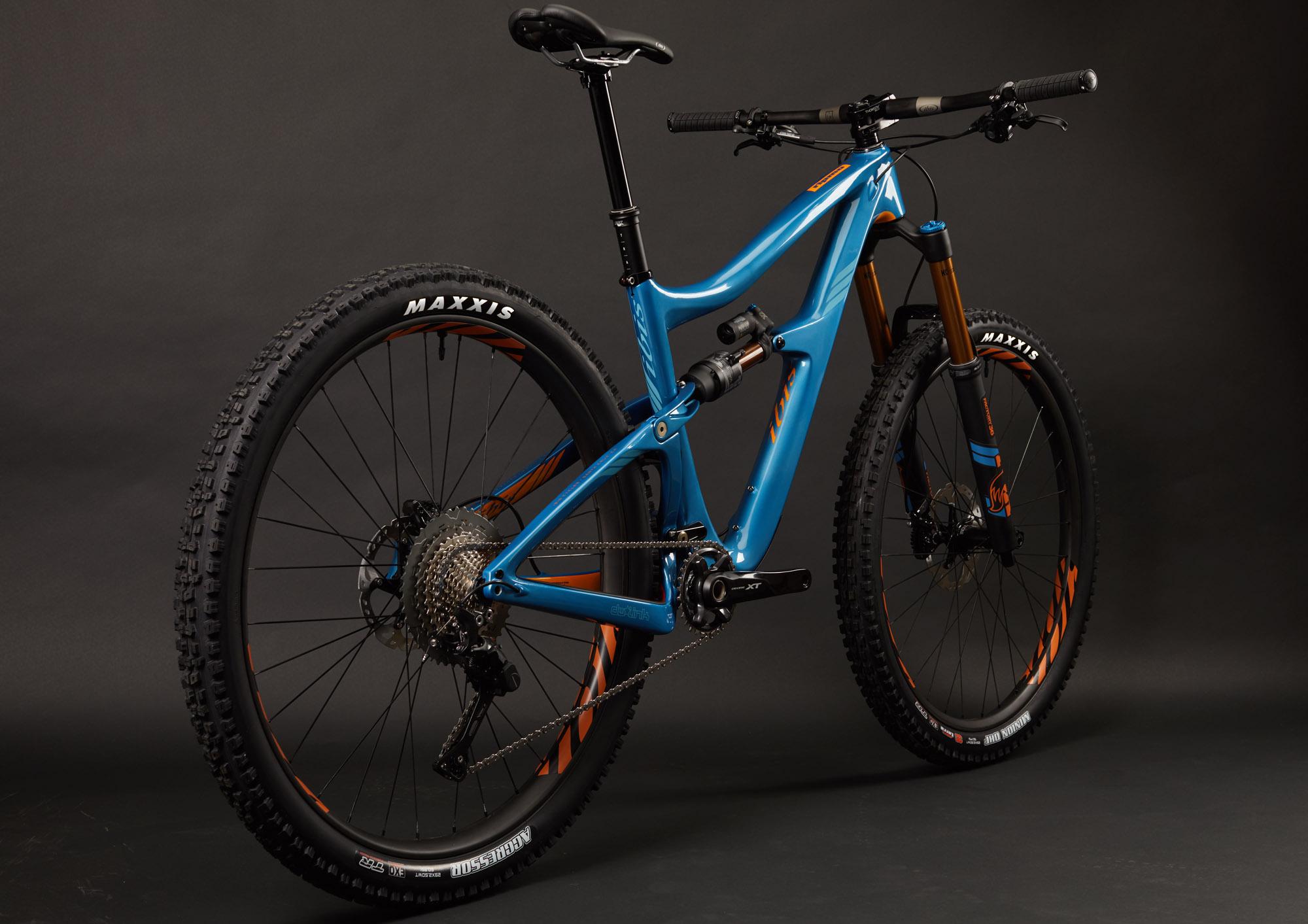 Ibis RipMo: A mountain bike featuring a vibrant blue frame with orange detailing, showcasing a rear and front suspension system, knobby tires branded with "Maxxis," and a modern design suitable for off-road cycling. The bike is positioned against a dark background, highlighting its sleek lines and intricate components.